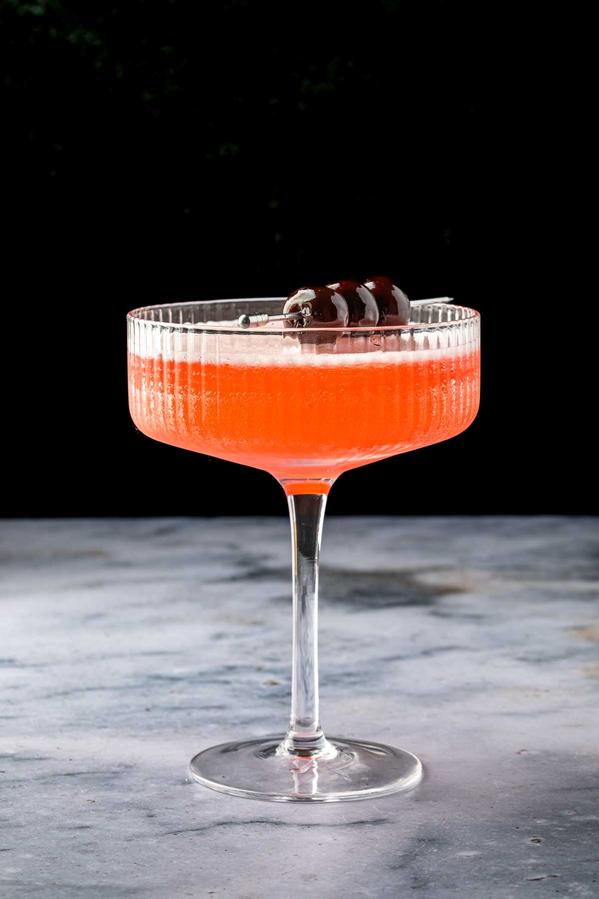 A pineapple, rum and cherry cocktail, garnished with cherries in a coupe glass. 