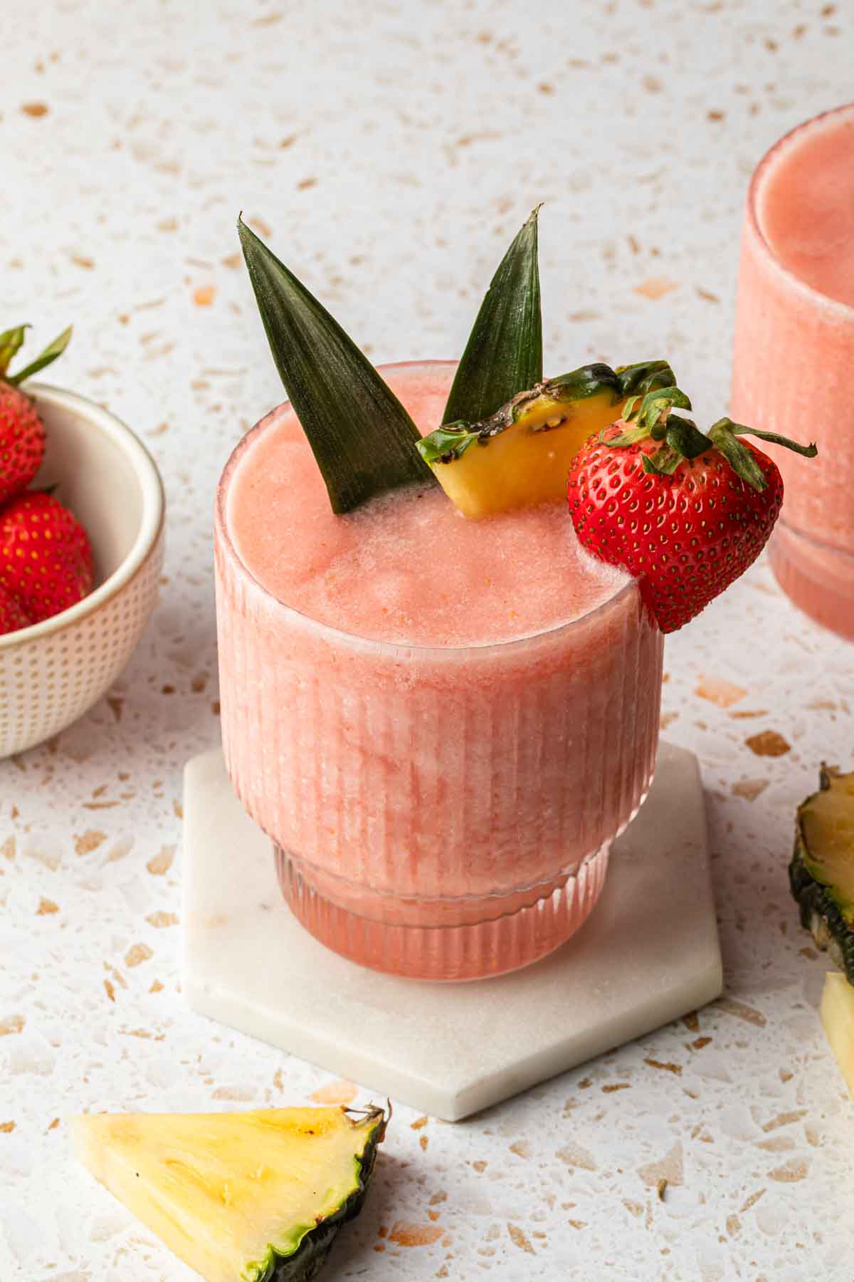 A frozen pink cocktail, garnished with pineapple and strawberry. 
