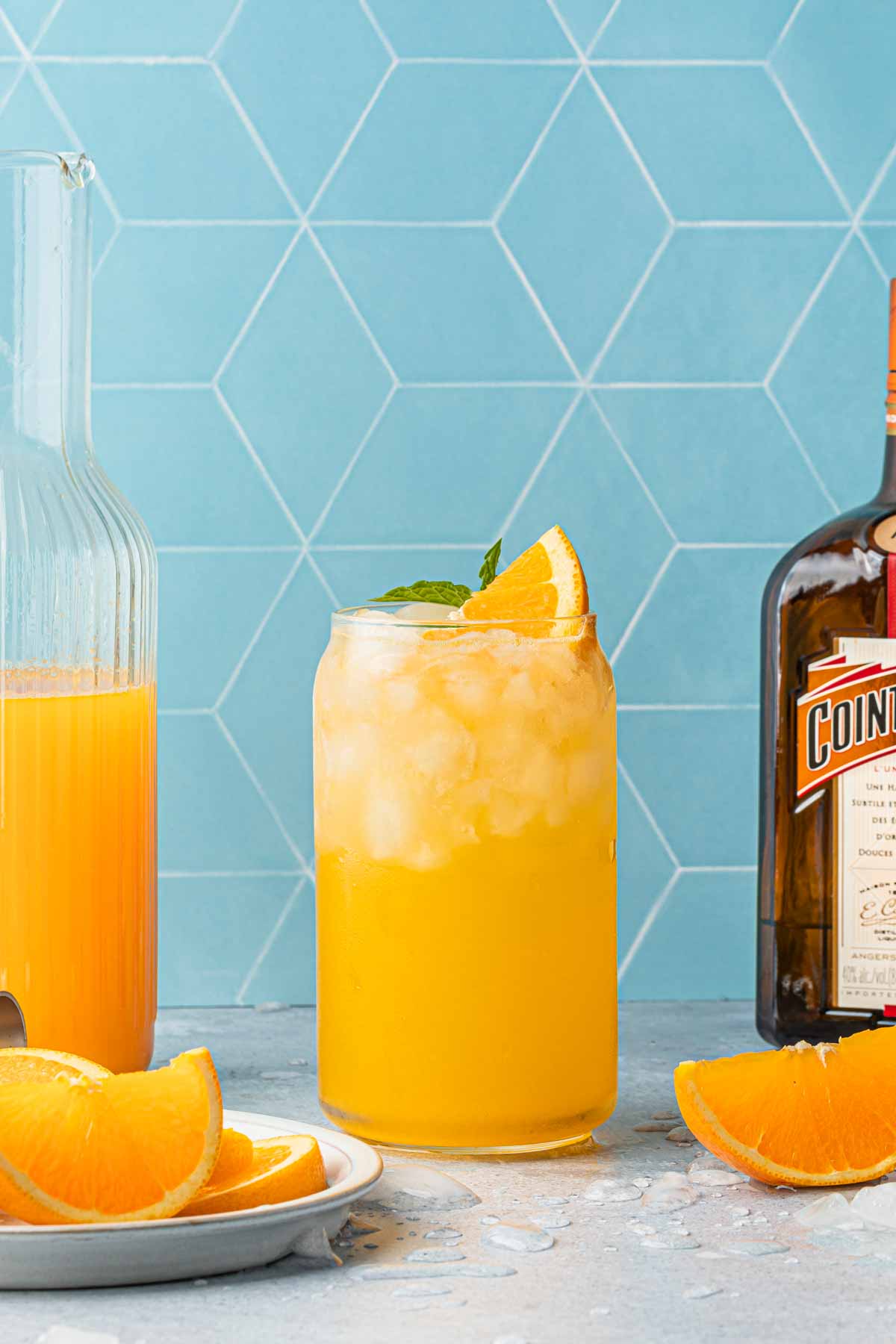 An orange crush cocktail in a can tumbler, garnished with an orange wedges next to a bottle of cointreau. 