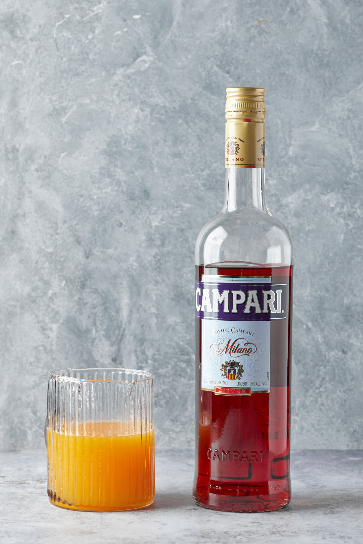 A small pitcher of orange juice and a bottle of campari sitting together. 