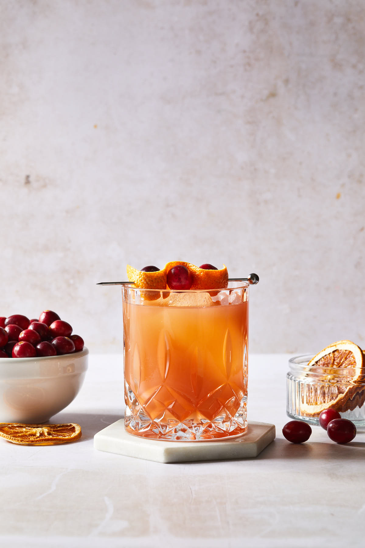 A cranberry orange whiskey sour garnished with cranberries and and orange peel. 