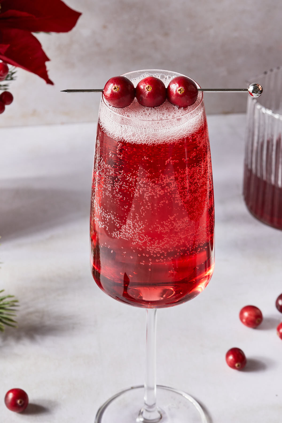 Close up of a cranberry mimosa in a champagne glass garnished with fresh cranberries. 