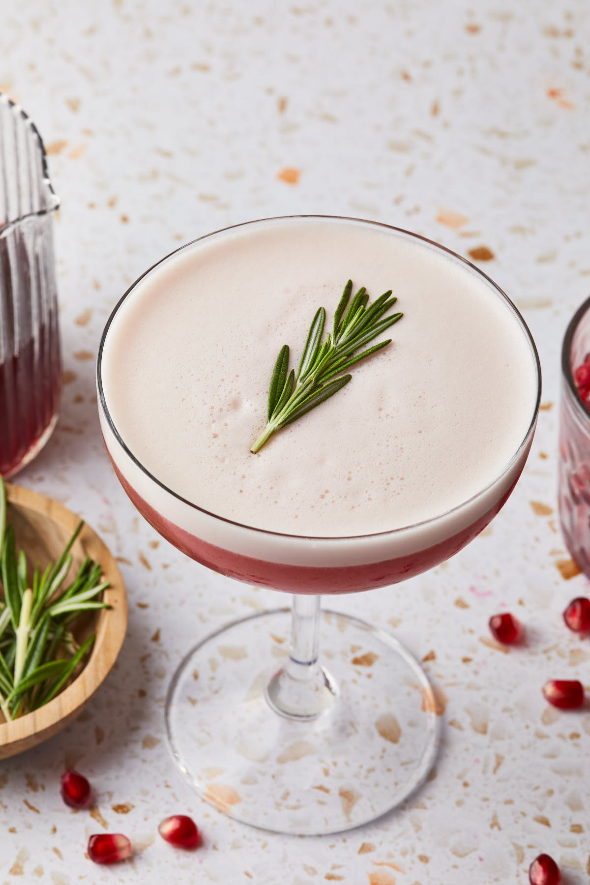 A rosemary pomegranate cocktail served in a coupe glass. 