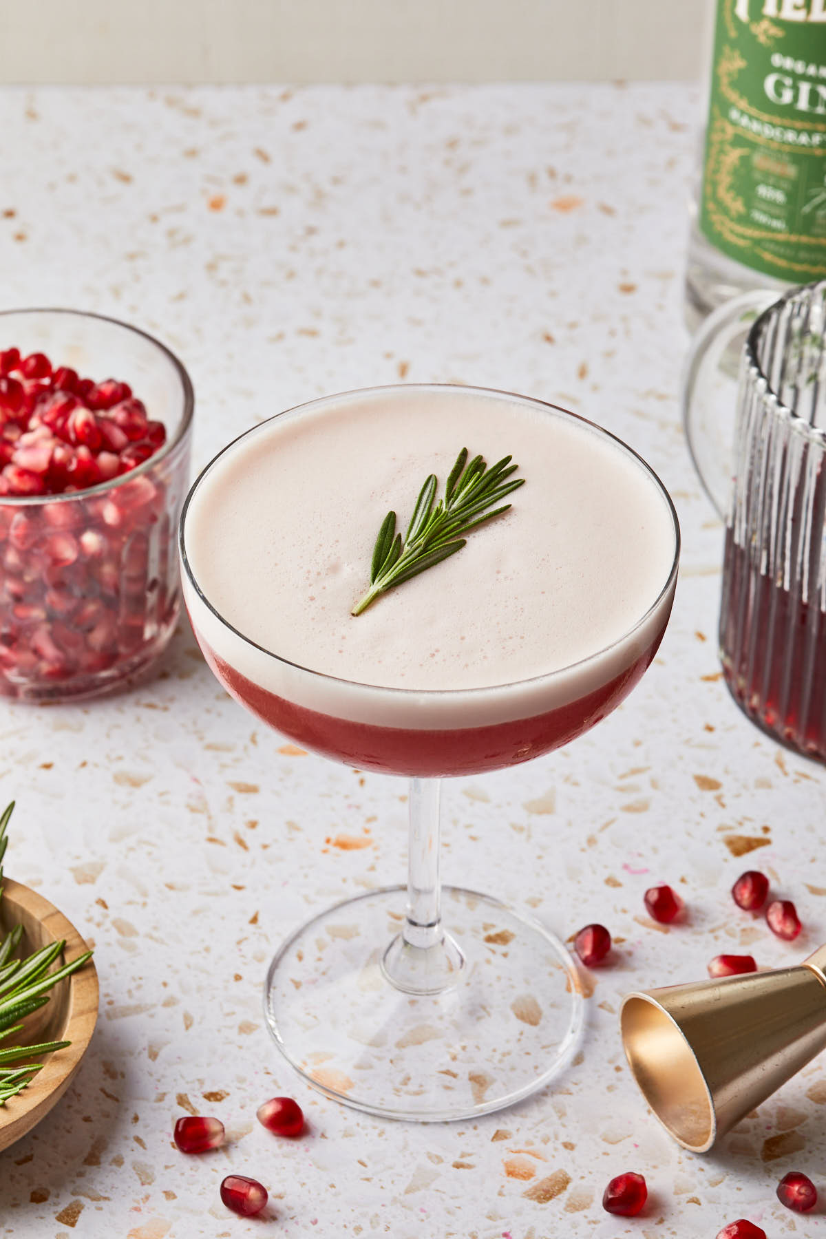 A rosemary pomegranate gin cocktail in a coupe glass. 