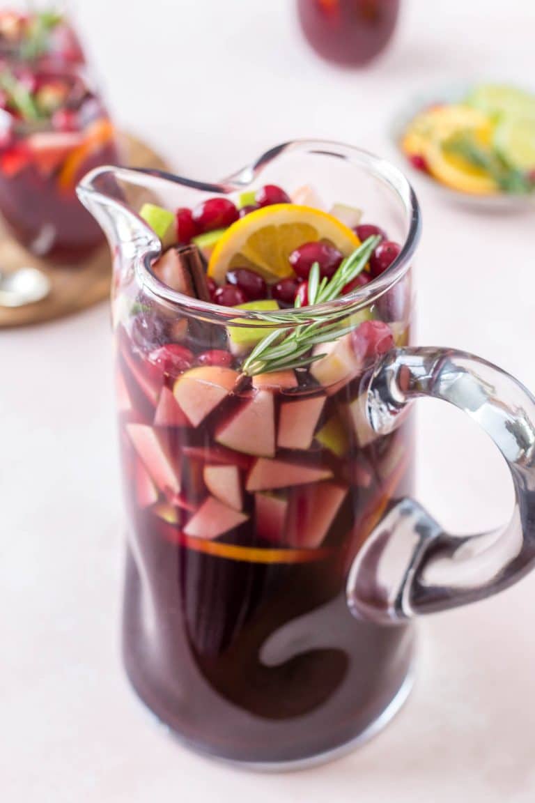 a pitcher of christmas sangria garnished with fruit, cinnamon stick and rosemary sprig