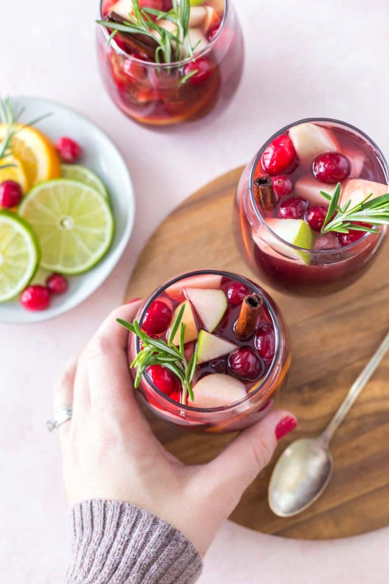 two glasses of christmas sangria, a hand taking one from a wooden tray