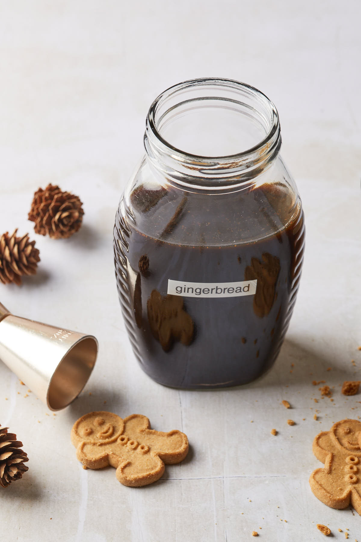 A cocktail mixer in a bottle surrounded by a cocktail jigger and some molasses holiday cookies. 