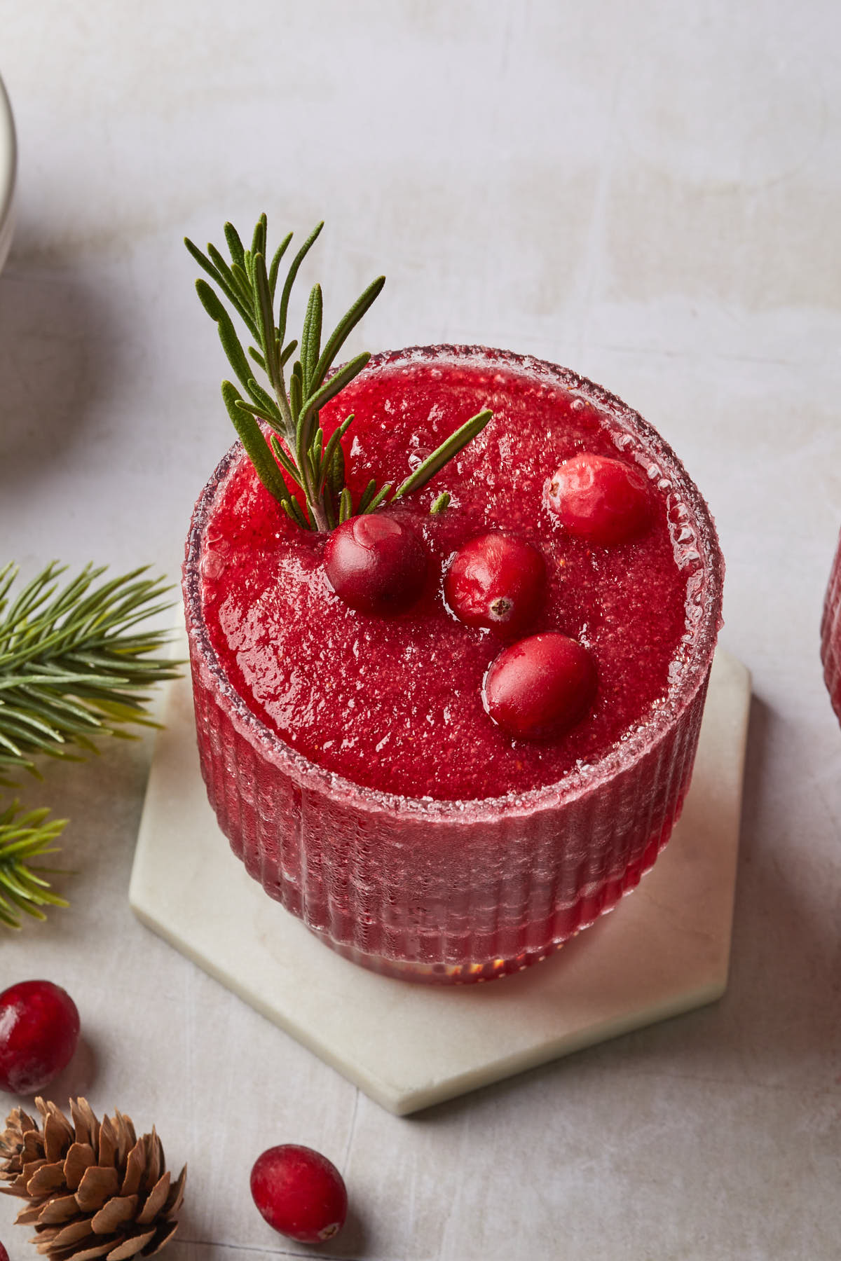 Close up of a christmas margarita in a sugar rimmed glass, garnished with fresh cranberries and a sprig of rosemary. 