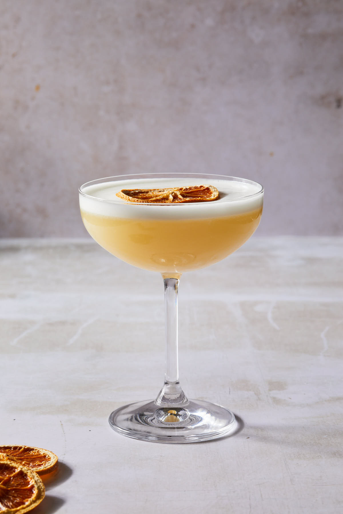 A tequila solstice cocktail in a coupe glass garnished with a dried orange wheel. 