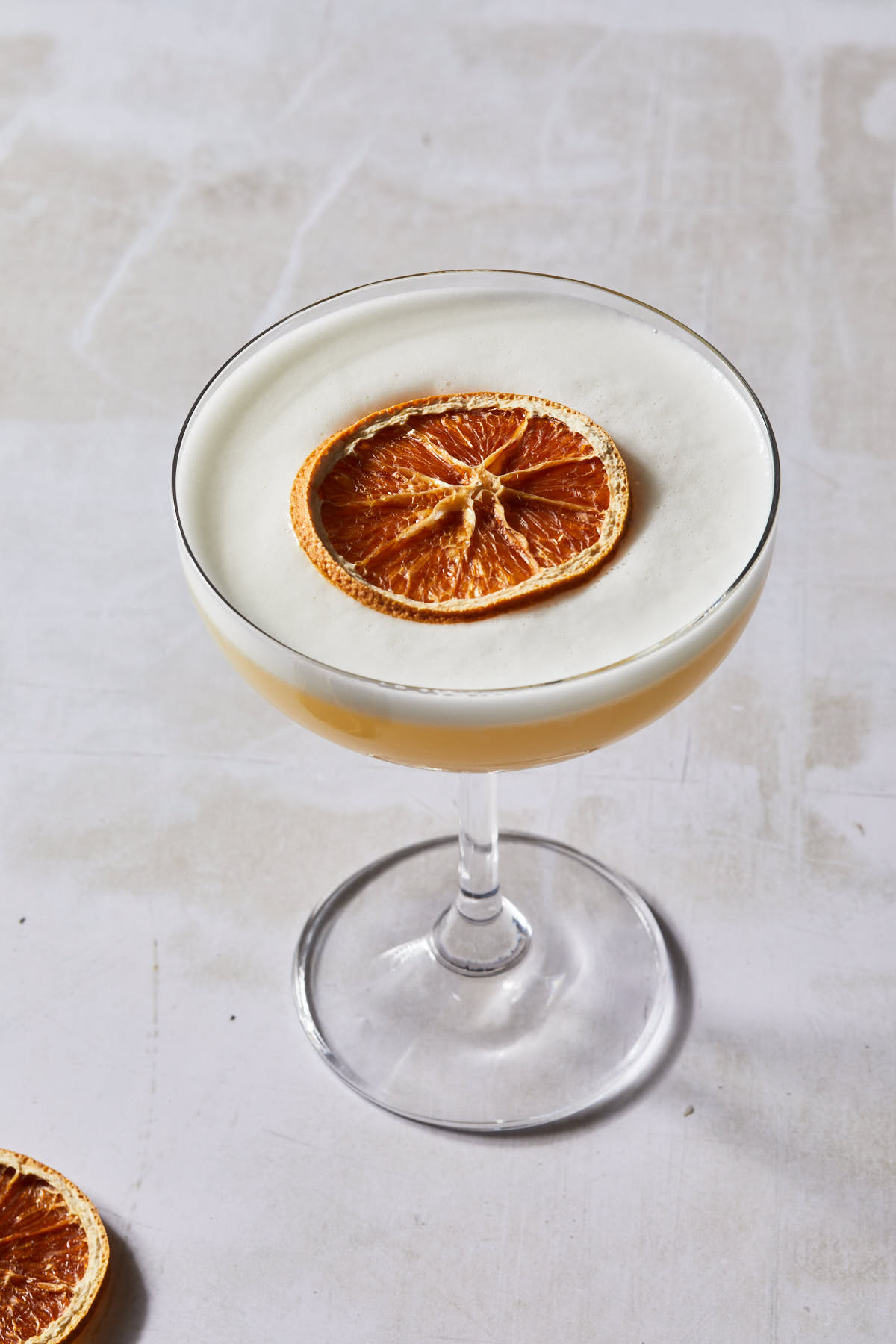 A coupe glass with a christmas tequila cocktail, garnished with a dried orange wheel. 