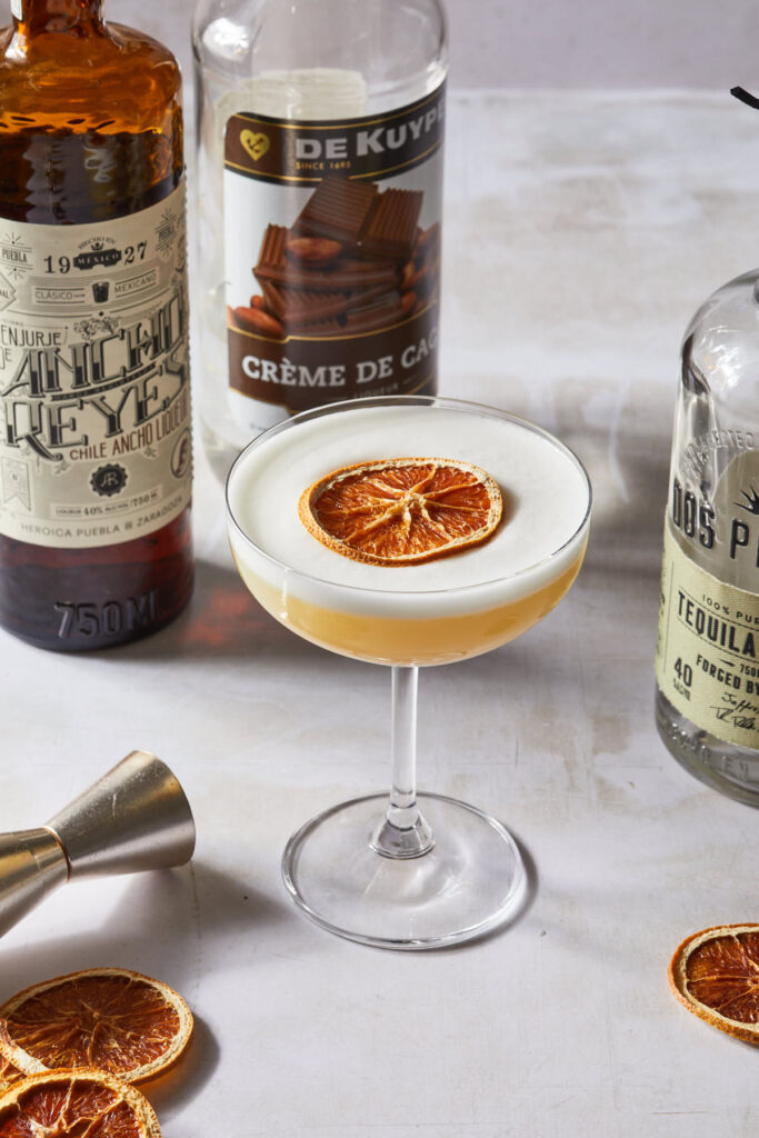 A coupe glass with a winter tequila cocktail, garnished with a dried orange wheel.