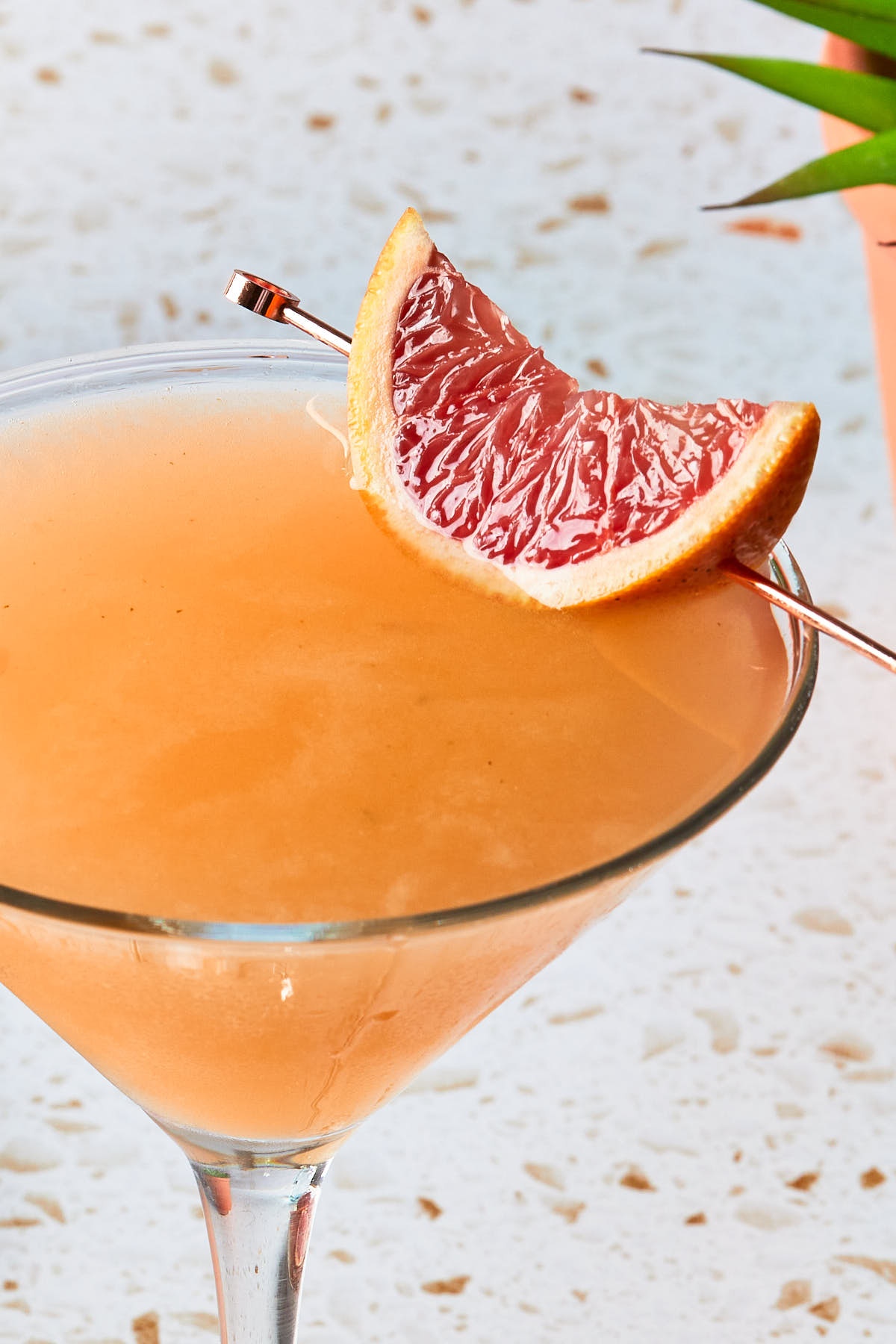 Close up of a grapefruit martini garnished with a grapefruit wedge. 