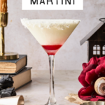 A coconut martini in a glass with a shredded coconut rim, featuring a red layer at the bottom. The background includes a red rose, books, a candle, a cocktail jigger, and a decorative house. Text reads “Coconut Martini.”.