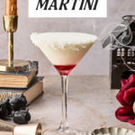 A coconut martini with a red layer sits on a marble surface, garnished with shredded coconut. Nearby are a candle, books, a rose, cocktail tools, and wisps of smoke. Text reads COCONUT MARTINI and Another Cocktail Blog.